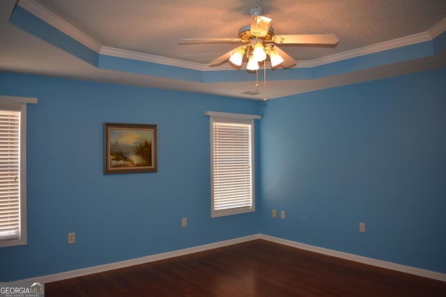 empty room with a tray ceiling, dark wood-style flooring, crown molding, and baseboards