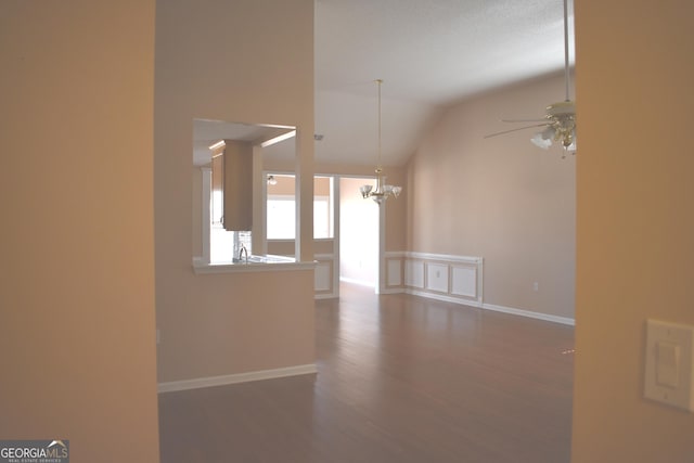 unfurnished living room featuring baseboards, lofted ceiling, wood finished floors, a sink, and ceiling fan with notable chandelier