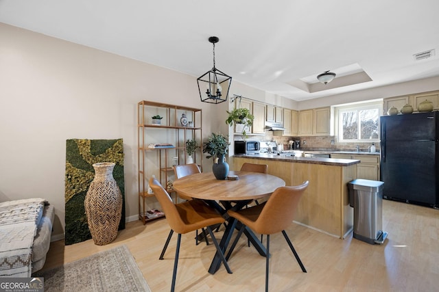 dining room with sink, a tray ceiling, light hardwood / wood-style flooring, and an inviting chandelier