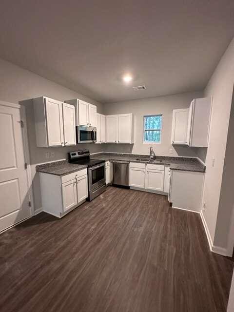 kitchen featuring dark wood-type flooring, sink, stainless steel appliances, and white cabinetry