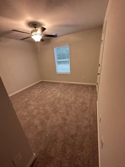 empty room with ceiling fan and dark carpet