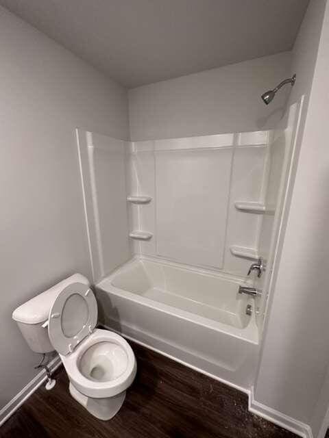 bathroom with toilet,  shower combination, and wood-type flooring