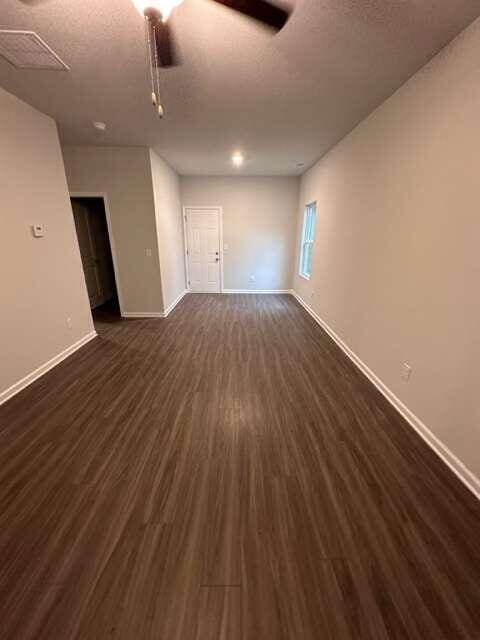 empty room with a textured ceiling, ceiling fan, and dark hardwood / wood-style flooring