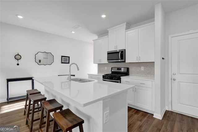 kitchen with white cabinets, stainless steel appliances, an island with sink, sink, and a breakfast bar