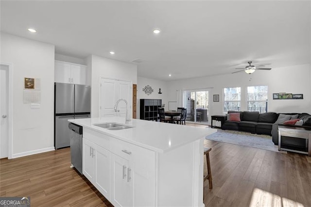 kitchen with ceiling fan, a center island with sink, sink, stainless steel appliances, and white cabinets