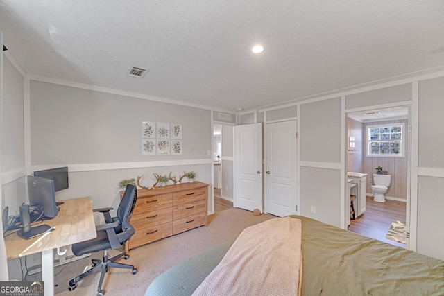 carpeted bedroom with ensuite bath, a textured ceiling, and ornamental molding