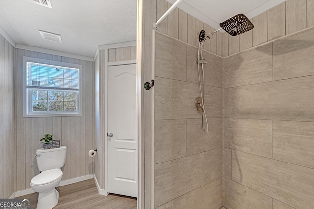 bathroom featuring toilet, wooden walls, hardwood / wood-style flooring, ornamental molding, and a tile shower