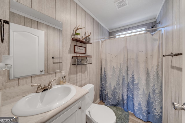 bathroom featuring toilet, wooden walls, walk in shower, ornamental molding, and vanity