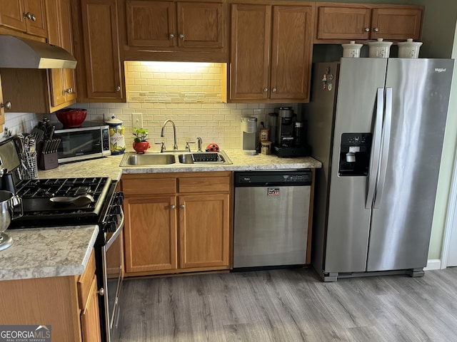 kitchen with light wood-type flooring, backsplash, sink, and stainless steel appliances