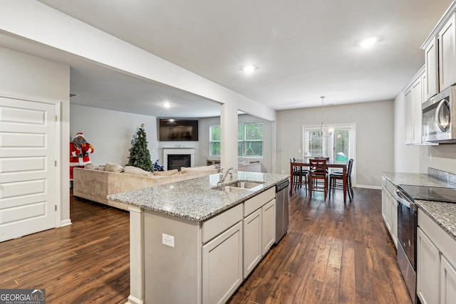 kitchen featuring appliances with stainless steel finishes, a kitchen island with sink, hanging light fixtures, light stone counters, and sink