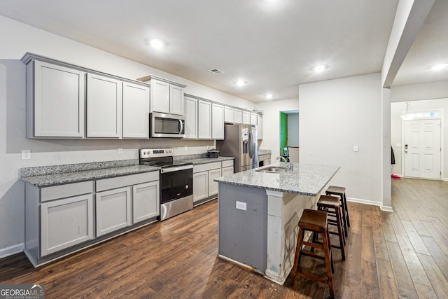 kitchen featuring appliances with stainless steel finishes, an island with sink, sink, gray cabinets, and light stone counters