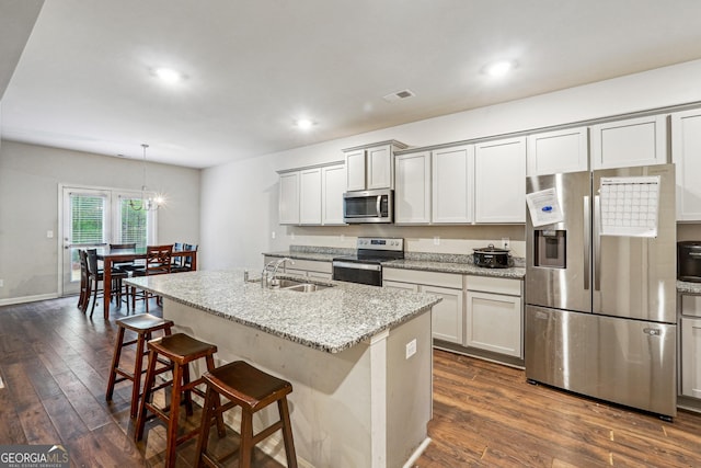 kitchen with a center island with sink, appliances with stainless steel finishes, pendant lighting, light stone counters, and sink