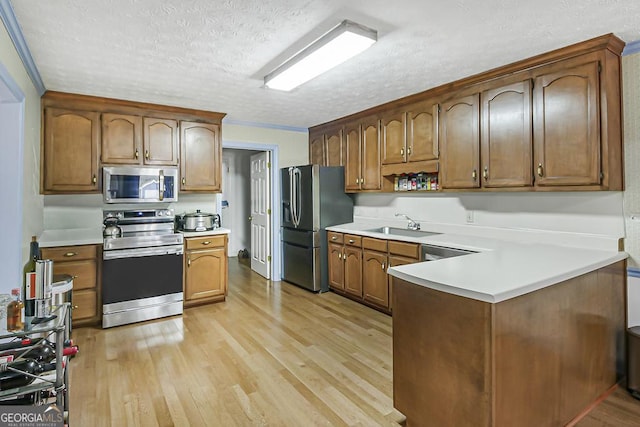 kitchen featuring a textured ceiling, stainless steel appliances, a peninsula, light countertops, and light wood-type flooring