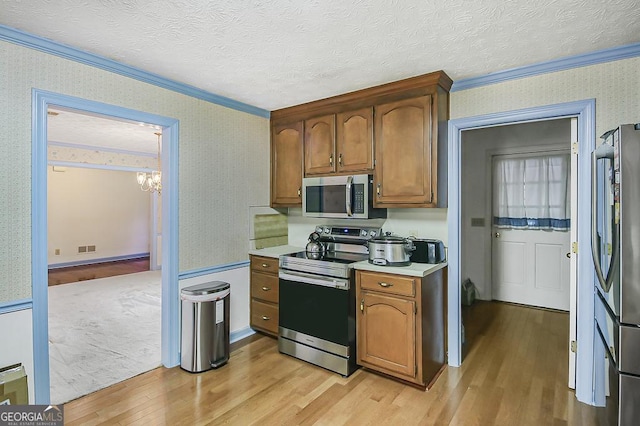 kitchen with crown molding, stainless steel appliances, light wood-style flooring, a textured ceiling, and wallpapered walls