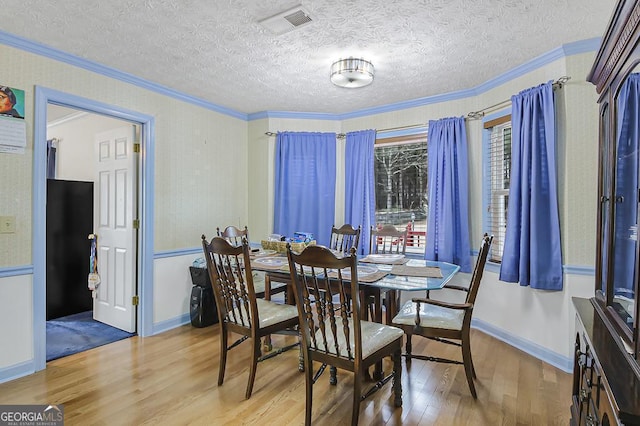 dining room featuring a textured ceiling, ornamental molding, baseboards, and light wood-style floors