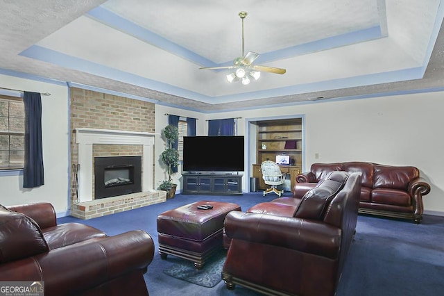 living room featuring ceiling fan, built in shelves, a fireplace, carpet, and a raised ceiling