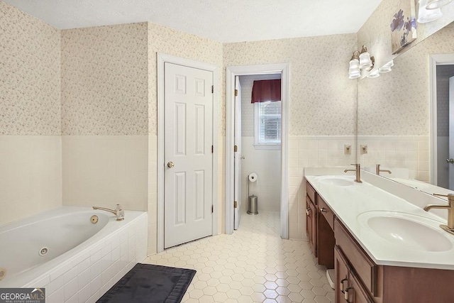 bathroom featuring a textured ceiling, wainscoting, a sink, and wallpapered walls