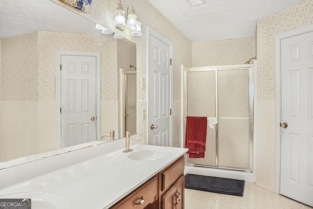 full bathroom with double vanity, wallpapered walls, tile patterned flooring, a shower stall, and a sink