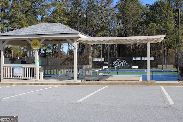 view of community with a tennis court, uncovered parking, a gazebo, and fence