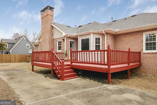 back of property featuring brick siding, roof with shingles, a chimney, fence, and a wooden deck