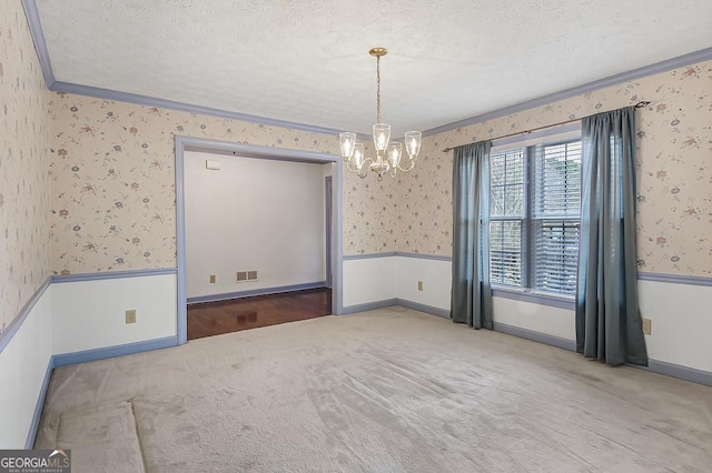 carpeted empty room featuring wallpapered walls, a textured ceiling, and a wainscoted wall