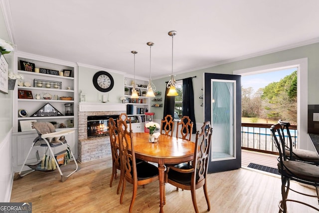 dining room featuring a brick fireplace, crown molding, a wealth of natural light, and light hardwood / wood-style floors