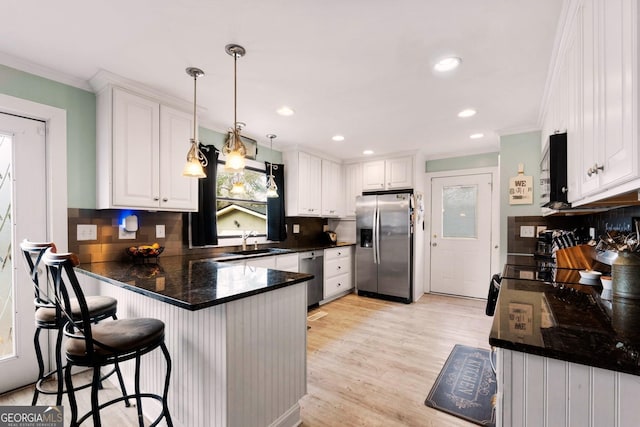 kitchen featuring white cabinets, dark countertops, a peninsula, stainless steel appliances, and a sink