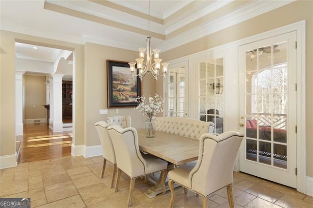 dining area featuring a tray ceiling, crown molding, a chandelier, and ornate columns