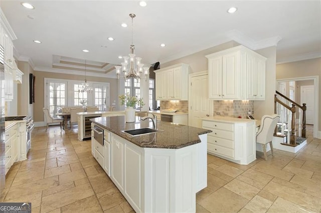 kitchen featuring decorative light fixtures, sink, an island with sink, ornamental molding, and a chandelier