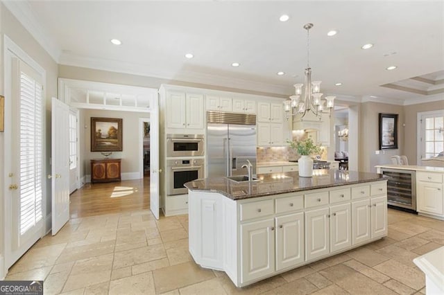 kitchen with white cabinetry, a center island with sink, appliances with stainless steel finishes, wine cooler, and hanging light fixtures