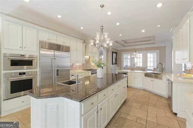 kitchen featuring sink, appliances with stainless steel finishes, a center island with sink, and a raised ceiling