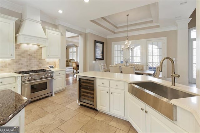 kitchen with beverage cooler, stainless steel range, white cabinetry, premium range hood, and sink