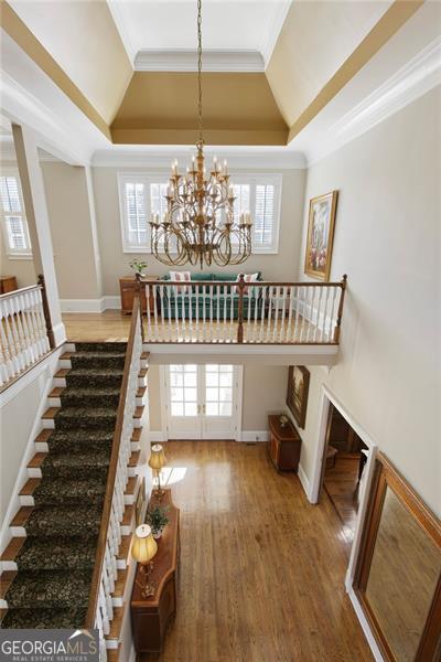 staircase with ornamental molding, a raised ceiling, wood-type flooring, and a notable chandelier