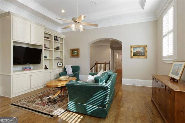 living room with ceiling fan, dark wood-type flooring, a raised ceiling, and ornamental molding