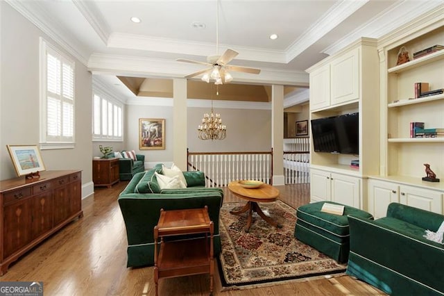 living room featuring ceiling fan with notable chandelier, ornamental molding, light hardwood / wood-style floors, and a tray ceiling