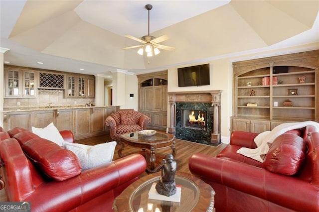 living room with lofted ceiling, ceiling fan, hardwood / wood-style floors, built in features, and a high end fireplace