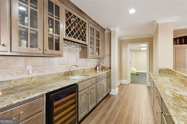 bar featuring beverage cooler, tasteful backsplash, sink, light stone counters, and crown molding