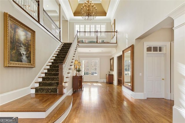 foyer with french doors, wood-type flooring, ornamental molding, and a towering ceiling