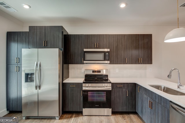 kitchen with pendant lighting, sink, light hardwood / wood-style flooring, stainless steel appliances, and dark brown cabinets