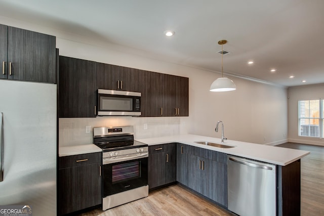 kitchen featuring appliances with stainless steel finishes, decorative light fixtures, light hardwood / wood-style floors, sink, and kitchen peninsula