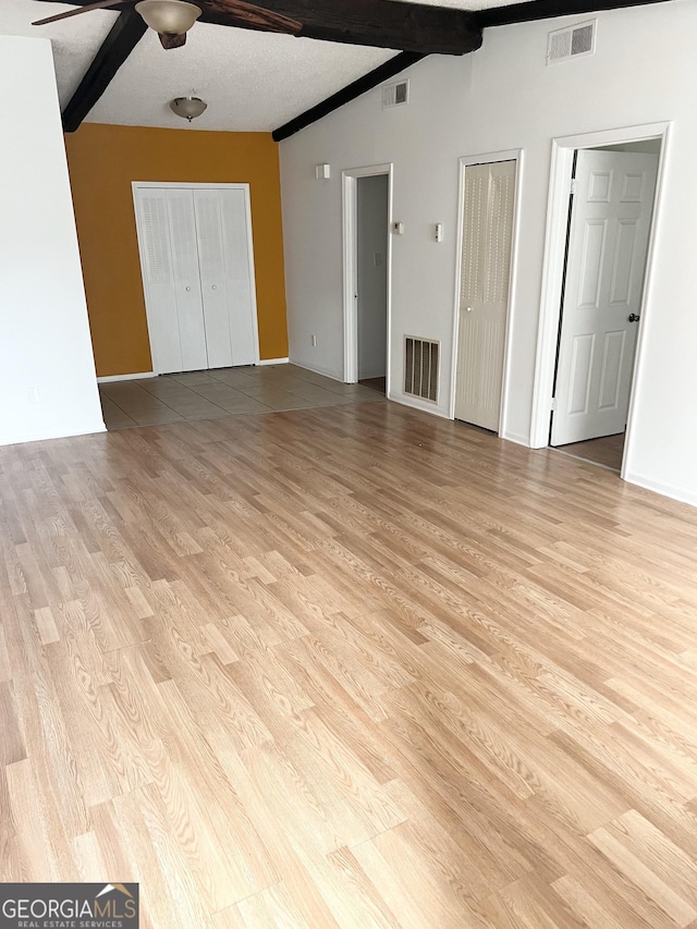 unfurnished bedroom with light wood-type flooring, ceiling fan, two closets, and lofted ceiling with beams