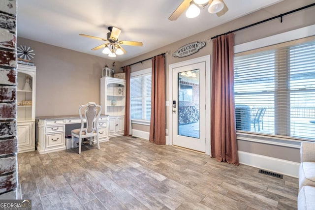 unfurnished office featuring ceiling fan, built in desk, and light hardwood / wood-style flooring