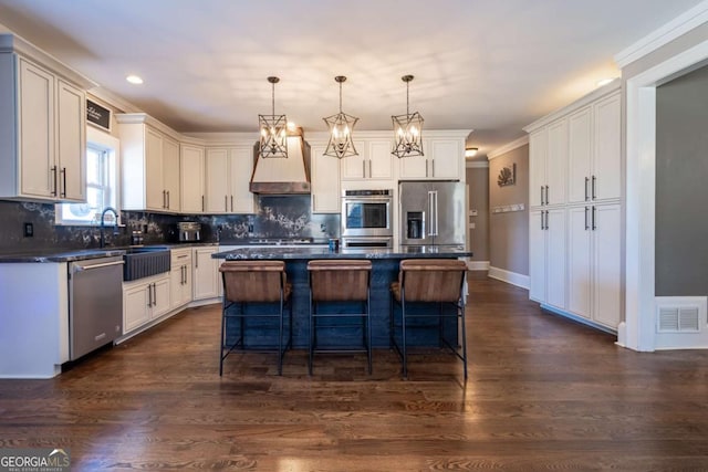 kitchen with custom exhaust hood, appliances with stainless steel finishes, a center island, hanging light fixtures, and sink