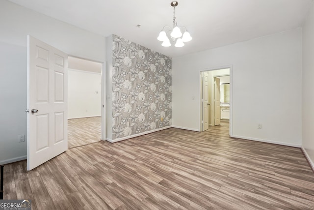 empty room with wood-type flooring and a notable chandelier