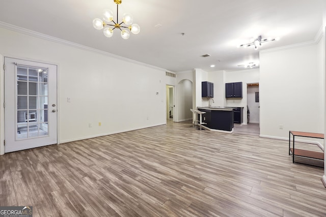 unfurnished living room with a notable chandelier, ornamental molding, and light hardwood / wood-style flooring