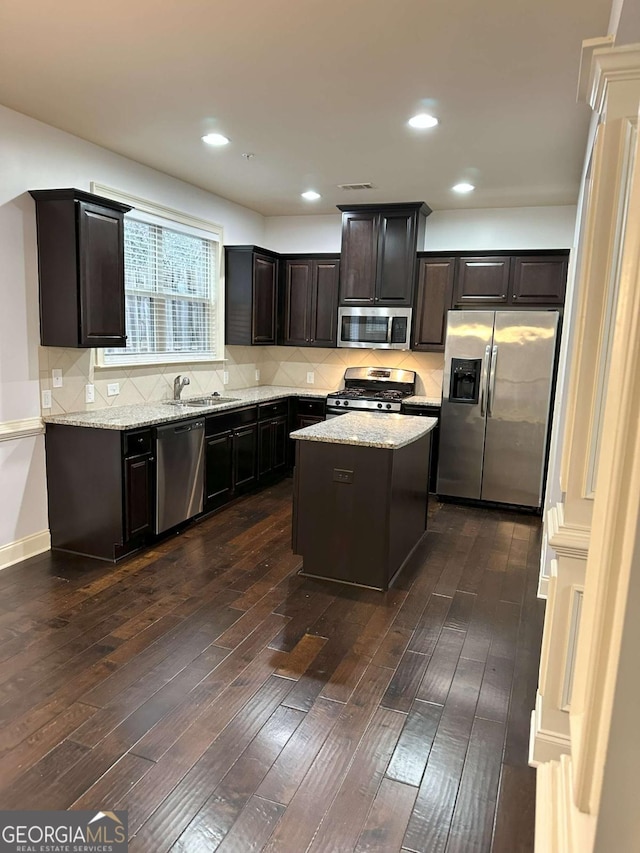 kitchen featuring dark hardwood / wood-style floors, a center island, sink, light stone countertops, and stainless steel appliances