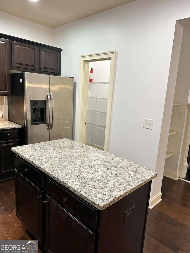 kitchen with light stone countertops, a kitchen island, stainless steel refrigerator with ice dispenser, dark wood-type flooring, and dark brown cabinets