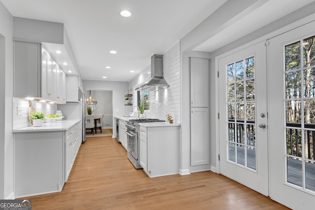 kitchen with high end stainless steel range oven, white cabinets, french doors, wall chimney exhaust hood, and light wood-type flooring