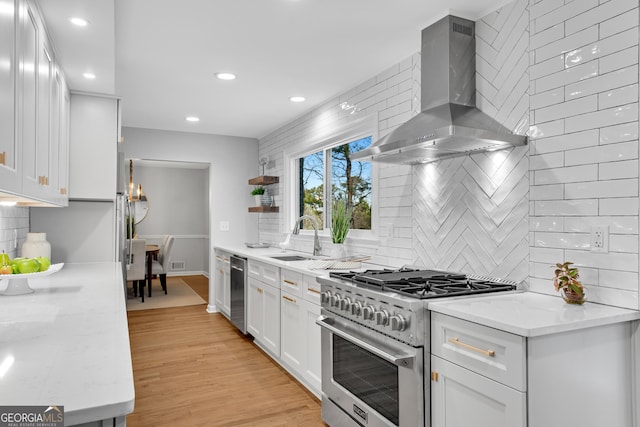 kitchen featuring sink, white cabinetry, stainless steel appliances, light stone countertops, and wall chimney range hood