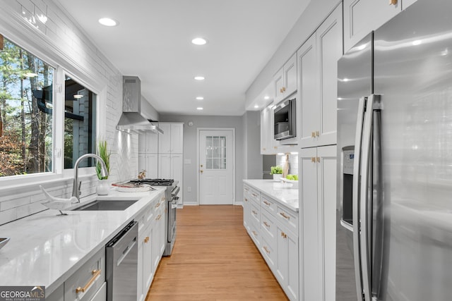 kitchen featuring white cabinetry, wall chimney range hood, stainless steel appliances, and sink